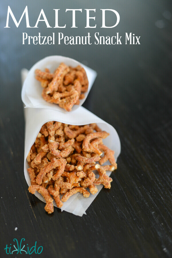 Two parchment cones filled with malted pretzel peanut snack mix on a dark wooden surface.