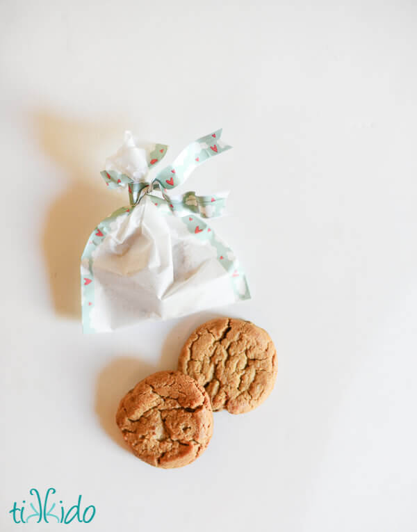 DIY favor bag made with parchment paper (so they're food safe) and decorated with washi tape, on a white surface next to two cookies.
