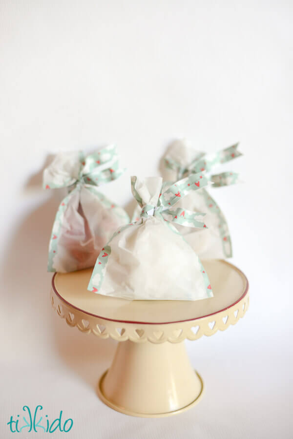 Three favor bags closed with washi tape twist ties, sitting on a cream colored cake stand.