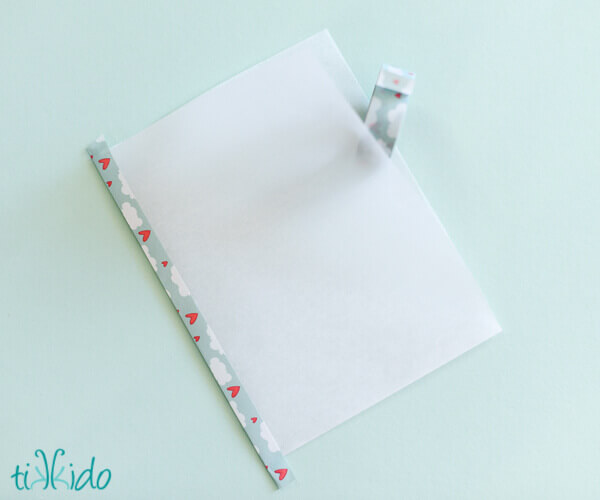 Parchment paper folded into a rectangle and being taped with washi tape to make a DIY food safe favor bag.