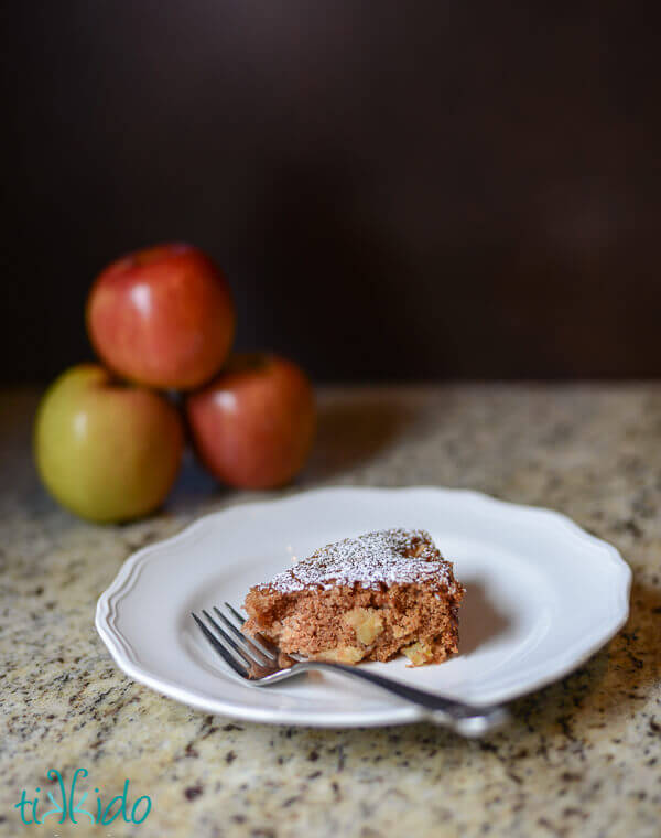 Apple cake dusted with powdered sugar on a white plate.