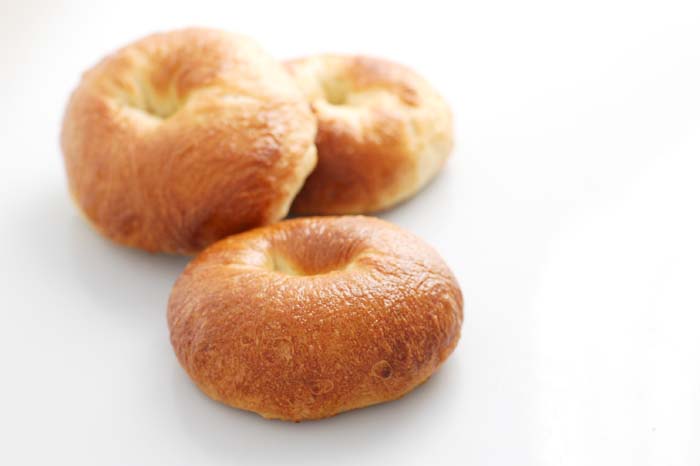 Three plain homemade bagels on a white surface.