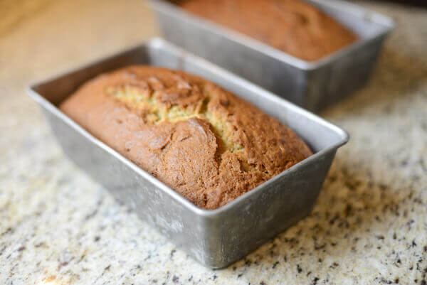 Two loaves of banana bread in pans on a granite counter.
