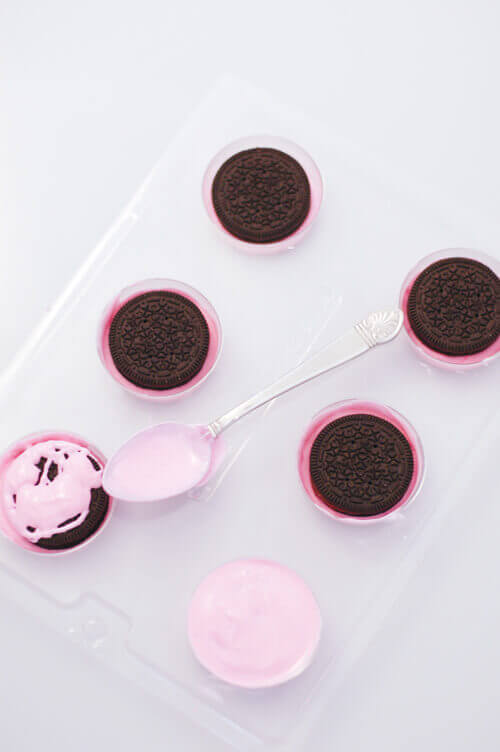 Oreos being covered with pink chocolate in a chocolate covered Oreo mold.