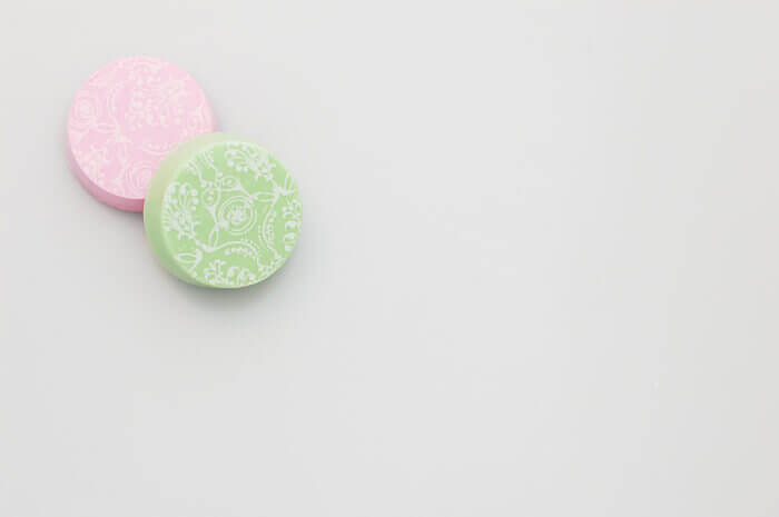 One pink and one green chocolate covered oreo with a delicate white pattern on top of the chocolate covered oreos.