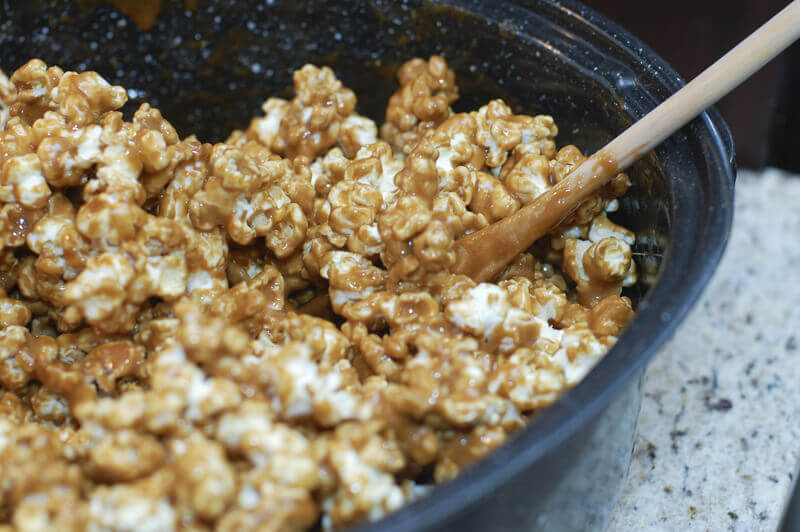 Caramel corn in a large roasting pan being stirred with a wooden spoon.