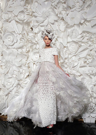 Model in a white floral dress in front of a giant white paper flower floral photo backdrop.