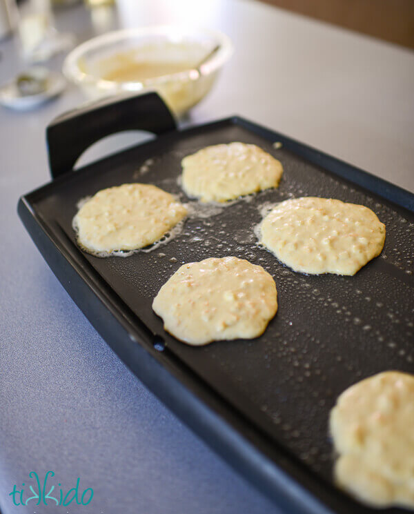 Savory cornmeal pancakes with cheddar cheese and corn cooking on an electric griddle.