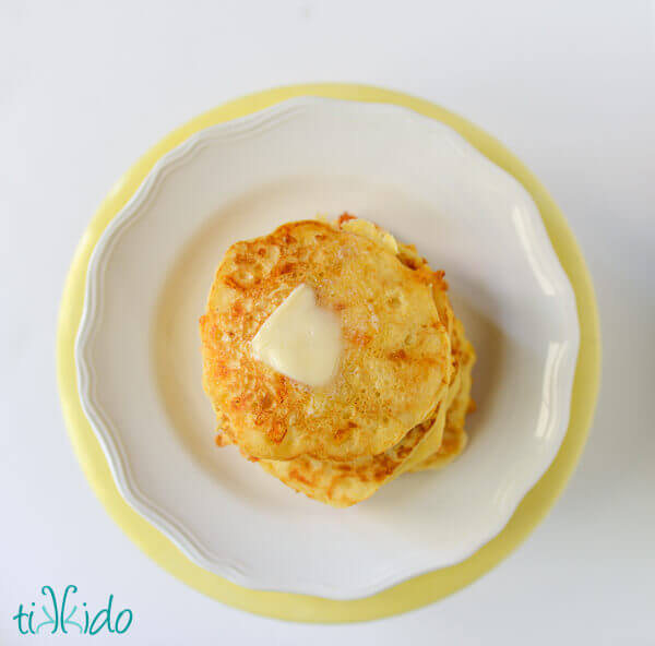 Savory pancakes made with cornmeal and cheddar stacked on a white plate, with a pat of butter melting on top.