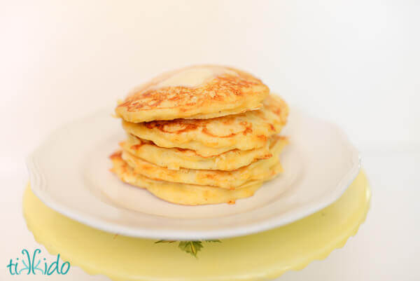 Savory cornmeal pancakes topped butter stacked on a white plate.