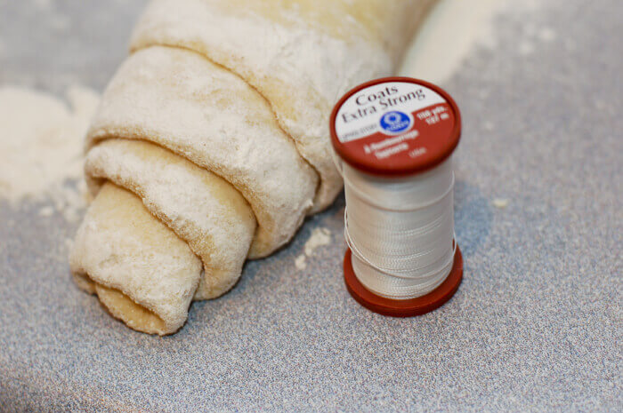 Cinnamon roll dough rolled into a log next to a spool of thread.