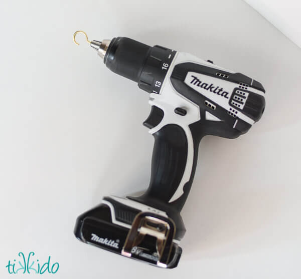 Black and white Makita drill on a white surface, with a hook instead of a drill bit.