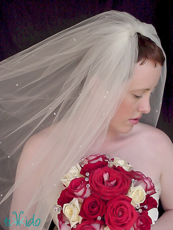 Bride holding a bouquet of red and white roses accented with clear crystal stems to add sparkle.