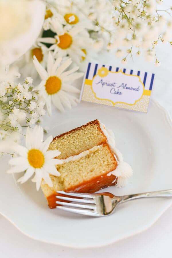 Slice of the BEST from scratch vanilla cake on a white plate surrounded by daisies and baby's breath flowers.