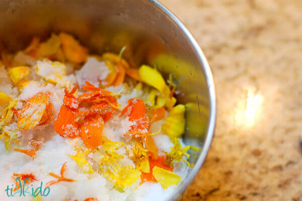 Marigold petals and sugar in a small saucepan on a granite surface.