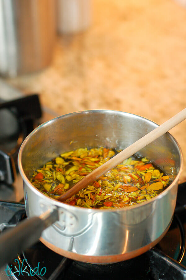 Marigold petals steeping in sugar water in a small pan on a gas stove, with a wooden spoon in the pot.