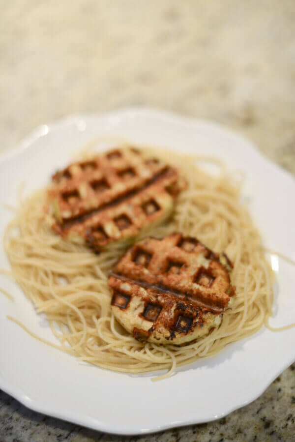 Low carb, gluten free, healthy eggplant parmesan made in a waffle iron on a bed of pasta on a white plate.