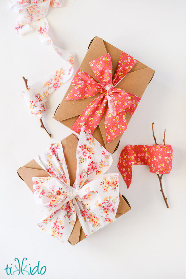 Two brown kraft boxes tied with homemade fabric ribbon bows, next to two spools of DIY fabric ribbon.