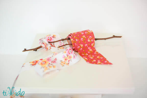 Two spools of DIY fabric ribbon wound around branches on a white background.