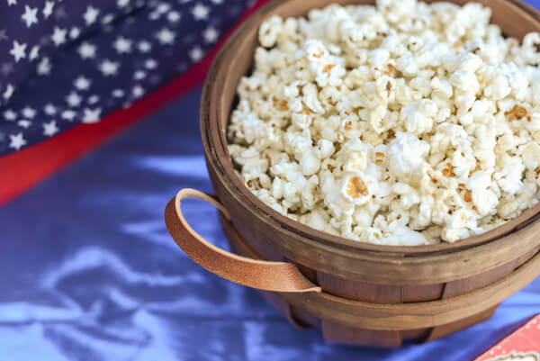 Rosemary parmesan popcorn in a wooden bowl on a blue fabric covered table.