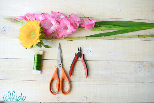 Fresh flowers, scissors, wire cutters, and green floral wire on a whitewashed wooden backdrop.