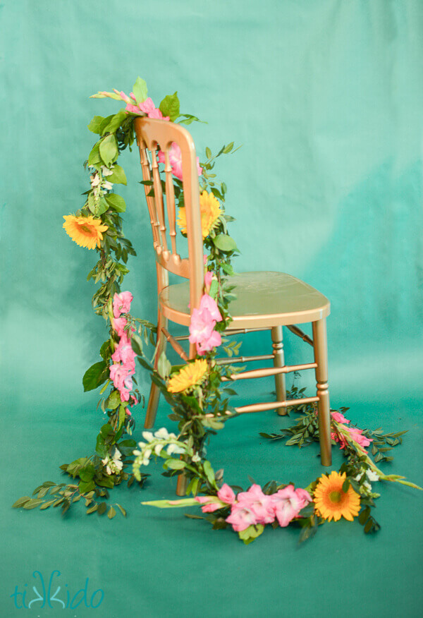 real flower garland draped on a golden chair on a turquoise background.