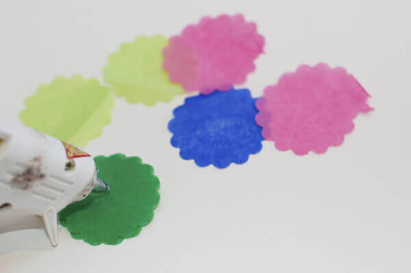 Scalloped circles of colorful tissue paper being glued together with a hot glue gun