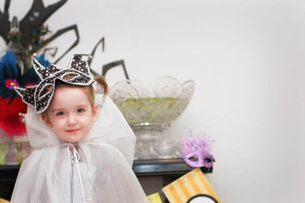 Little girl wearing a white tulle cape and a black and white masquerade mask.