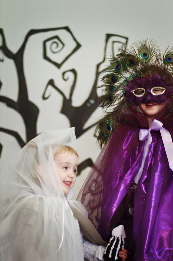 Two young girls wearing tulle capes, one purple, one a ghostly white color.