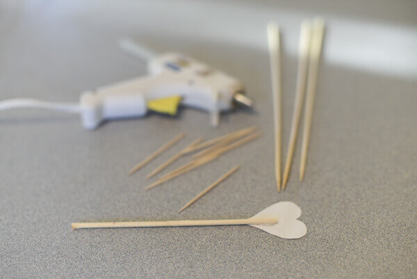 Paper hearts being glued to bamboo skewers to create a Valentine's Day Cake Topper.