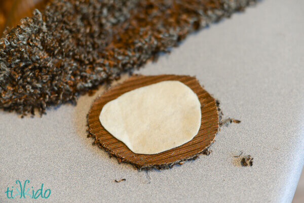 Curly brown fake fur fabric being cut to shape and glued to felt base to make DIY hobbit feet flip flops.