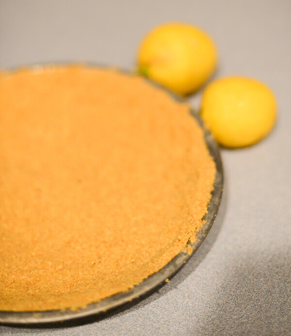 Graham Cracker crust pressed into a pie tin for making a lemon pie.  Two whole lemons sit beside the  pie tin.