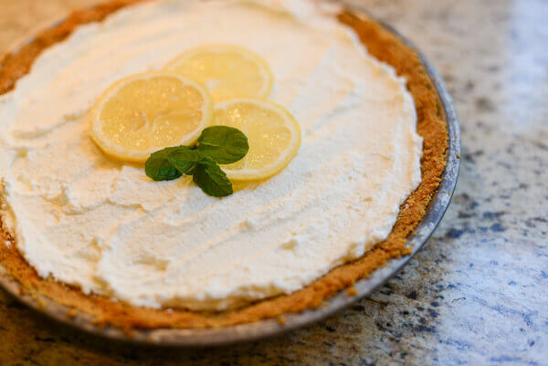 Chilled lemon pie topped with a whipped cream layer, and garnished with slices of fresh lemon and a sprig of mint.