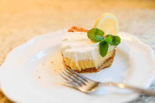 Half eaten slice of lemon custard pie on a white plate.