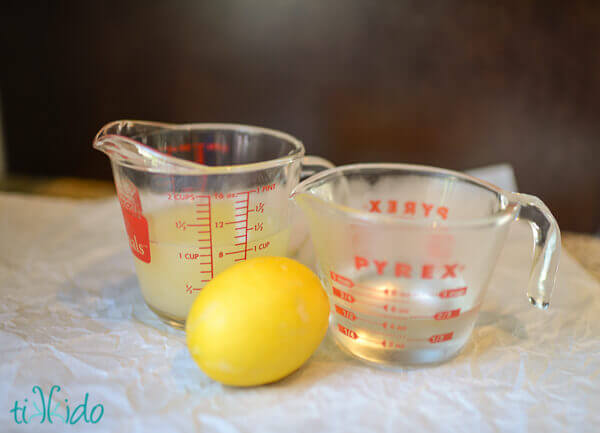 Lemon next to two pyrex measuring cups, one with simple syrup, one with lemon juice.