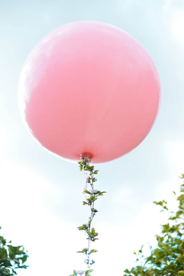 Large round pink balloon with a floral garland string floating in the air