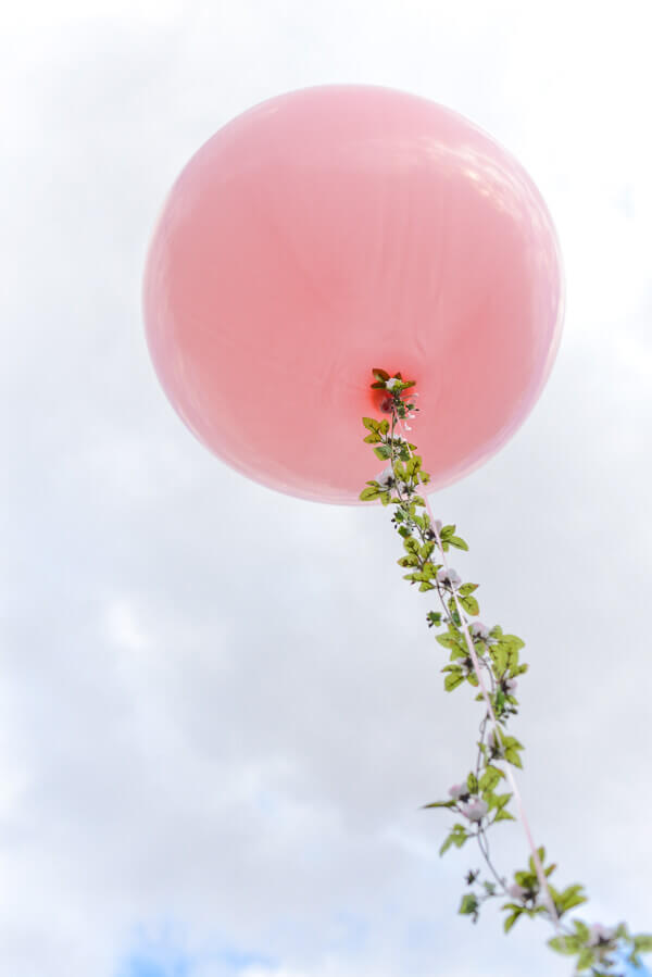 Large round pink balloon with a floral garland string floating in the air
