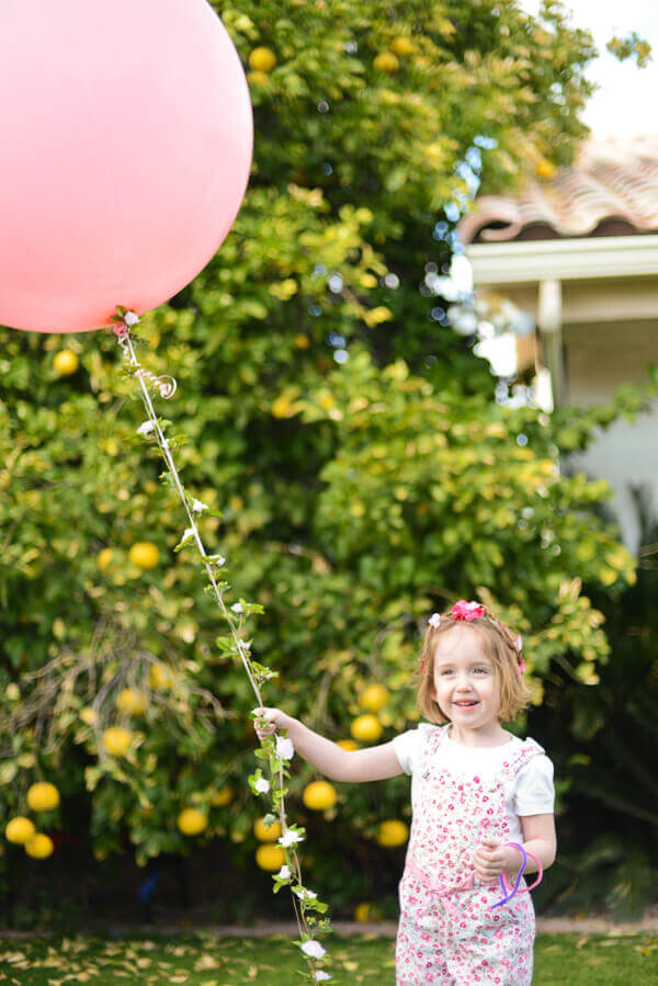 Large round pink balloon with a floral garland string held by a small girl with a flower crown.