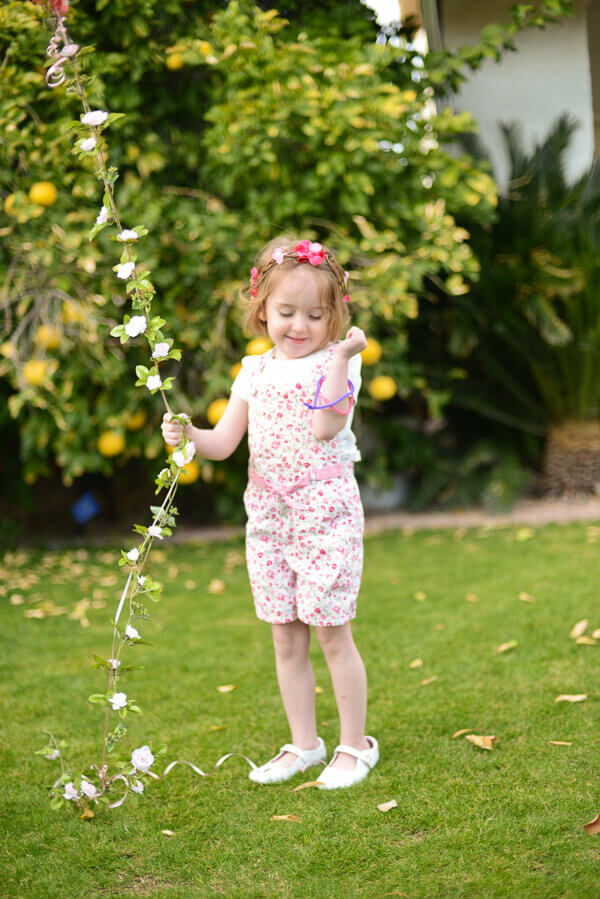 Large round pink balloon with a floral garland string held by a small girl with a flower crown.