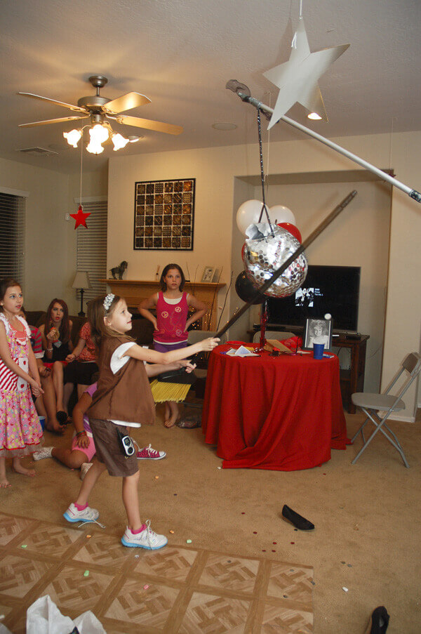 Piñata that looks like a disco ball hanging from the ceiling being hit by a child with a stick
