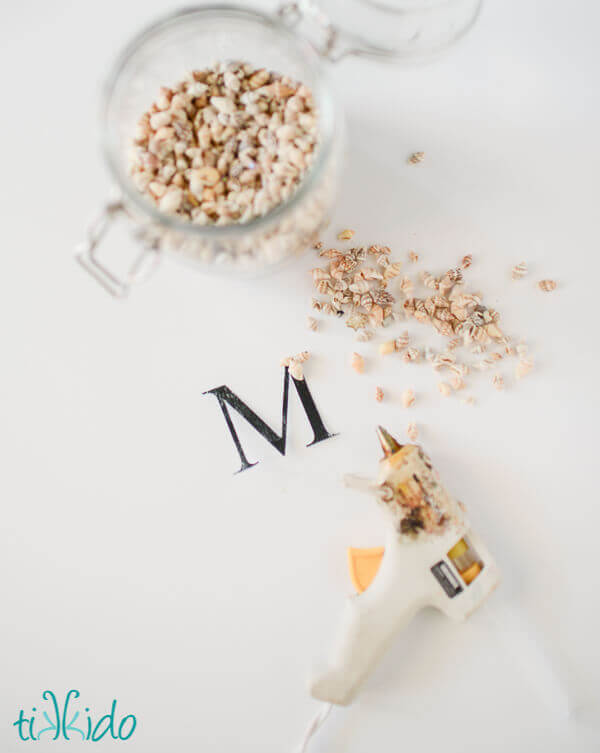 Tiny shells being glued on a letter M cut out of card stock to make a Nautical Monogram Cake Topper.