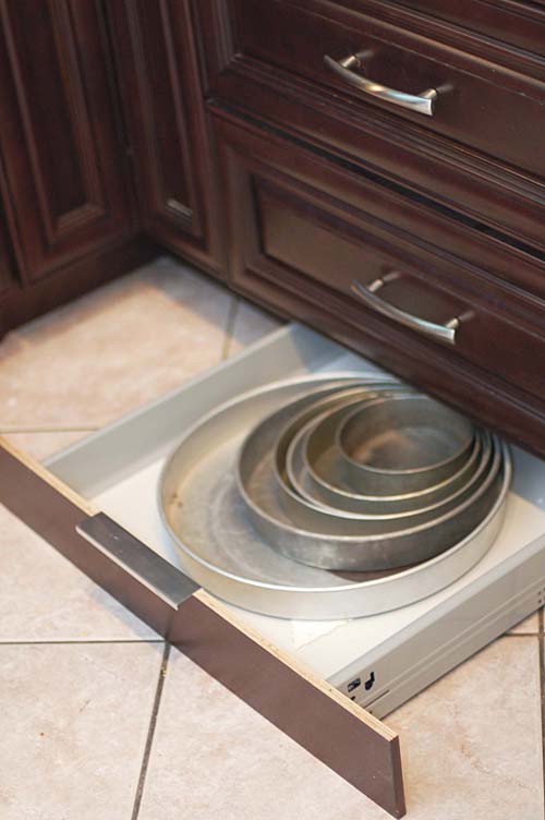Cake pans in a toe kick drawer under brown kitchen cabinets.