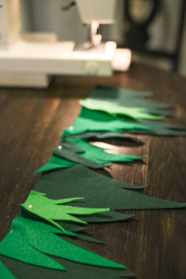 Jagged triangles of green felt in three different shades pinned together in a line, sewing machine in the background.