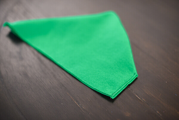 Green felt peter pan hat sewn together, but not yet with the brim turned up, on top of a dark brown wooden surface.