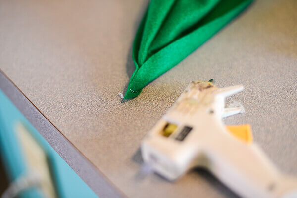 Front tip of a green felt peter pan hat next to a low temperature hot glue gun.