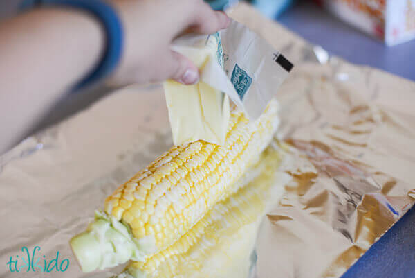 corn being buttered on aluminum foil