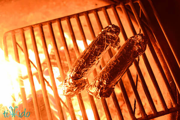 Ears of corn wrapped in foil being grilled over a campfire