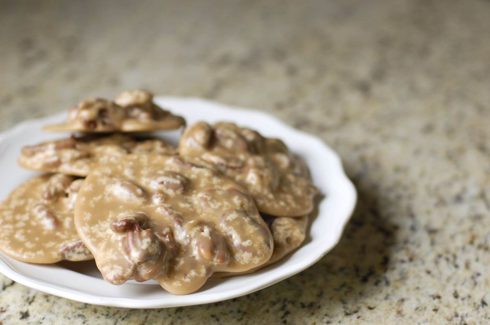 A white plate stacked with New Orleans pralines on a granite counter.