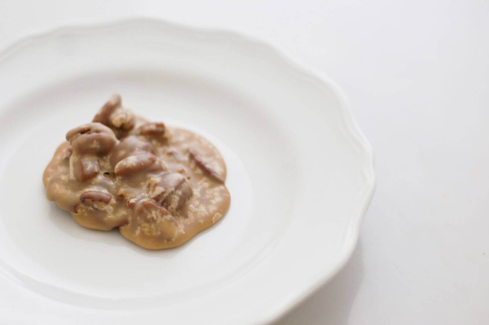 A single pecan praline sitting on a white plate.