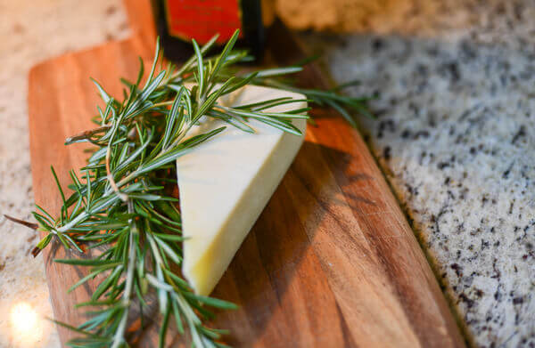 Fresh rosemary and parmesan cheese on a wooden cutting board for making Rosemary Parmesan Popcorn